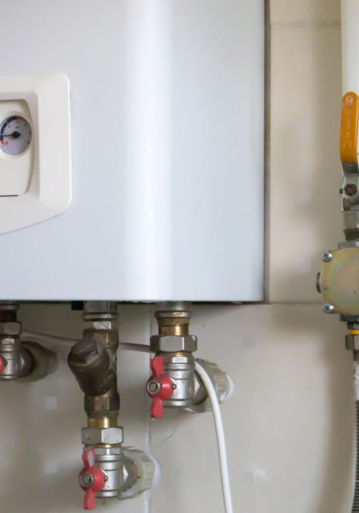 A gas double-circuit boiler is installed in the apartment. Autonomous heating boiler with a control panel, buttons, a display with temperature readings and red valves on pipes in a home kitchen