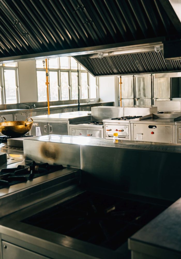 Professional kitchen in modern restaurant displays a shiny metal bowl on stove. Clean arrangement of equipment chrome appliances and new furniture. Bright gas service is working.