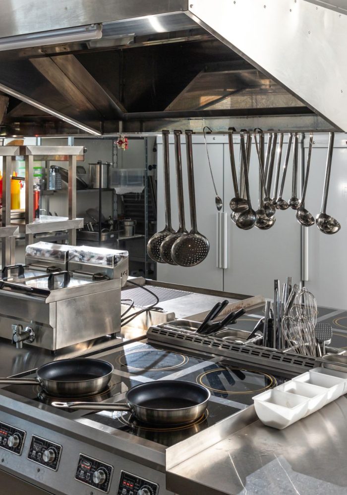 Modern shiny kitchen with stainless still kitchenware and equipment for restaurant-scale cooking with preparation tables, pans, pots, stoves